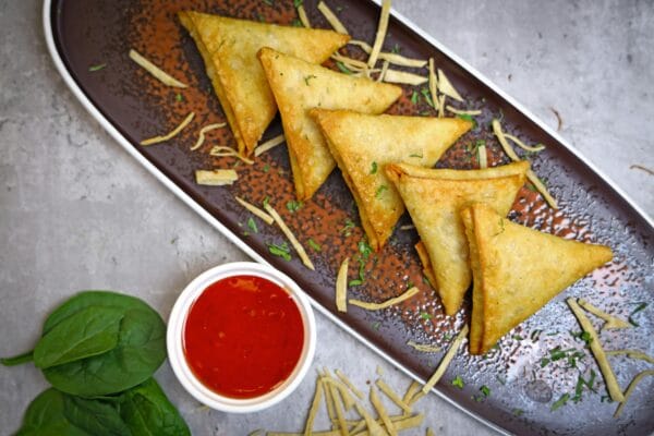 Delicious crispy samosas served with spicy red sauce on a platter.