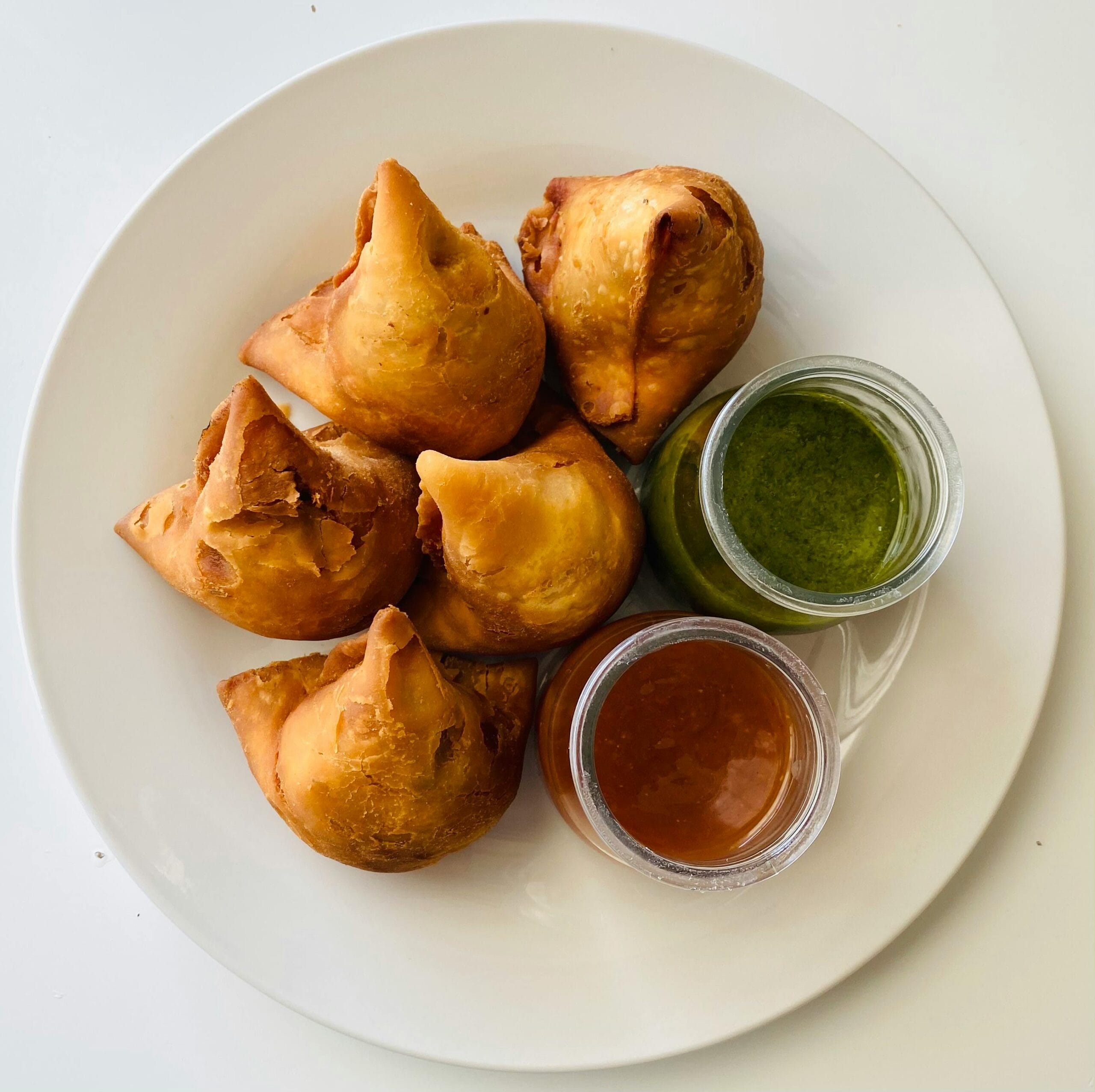 pexels photo 9027521 9027521 Top view of crispy samosas served with green and tamarind chutneys on a white plate.